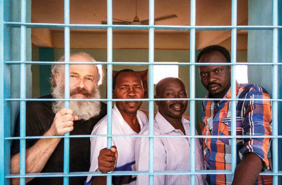 four men stand behind bars in a jail cell